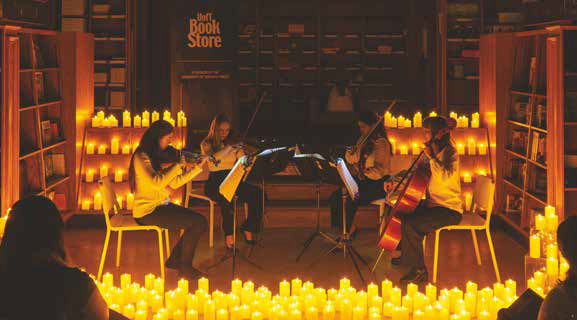 Photo of a string quartet playing in UofT bookstore, surrounded by many lit candles
