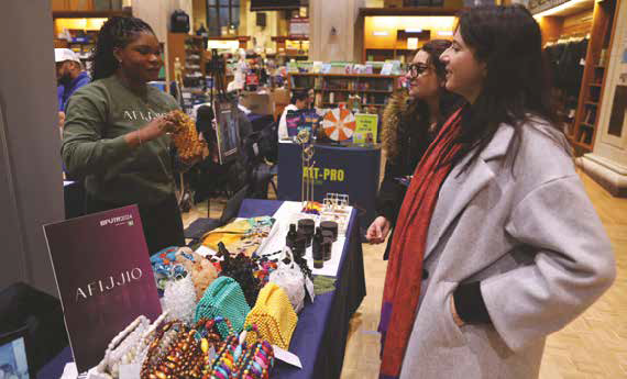 Photo of a person showing AFIJJIO merchandise to two people