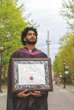 Photo of a UofT graduate holding a certificate in front of the CN tower
